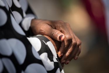 African woman's hands folded in her lap, as she wears a black and white dress. 